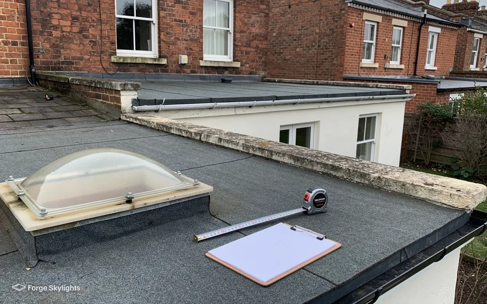A dome rooflight on a felt flat roof with a clipboard and tape measure beside it