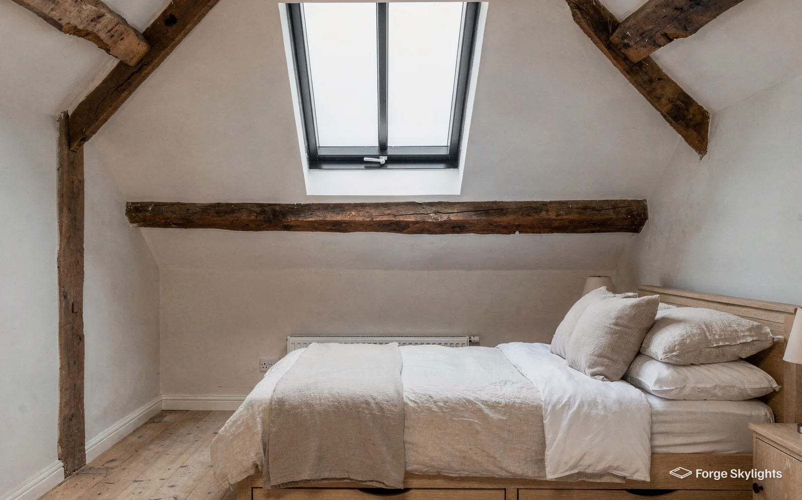 A bedroom with oak beams and a conservation rooflight above the bed