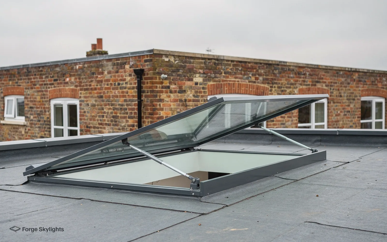 An opening rooflight propped open on a flat roof with a brick building behind it