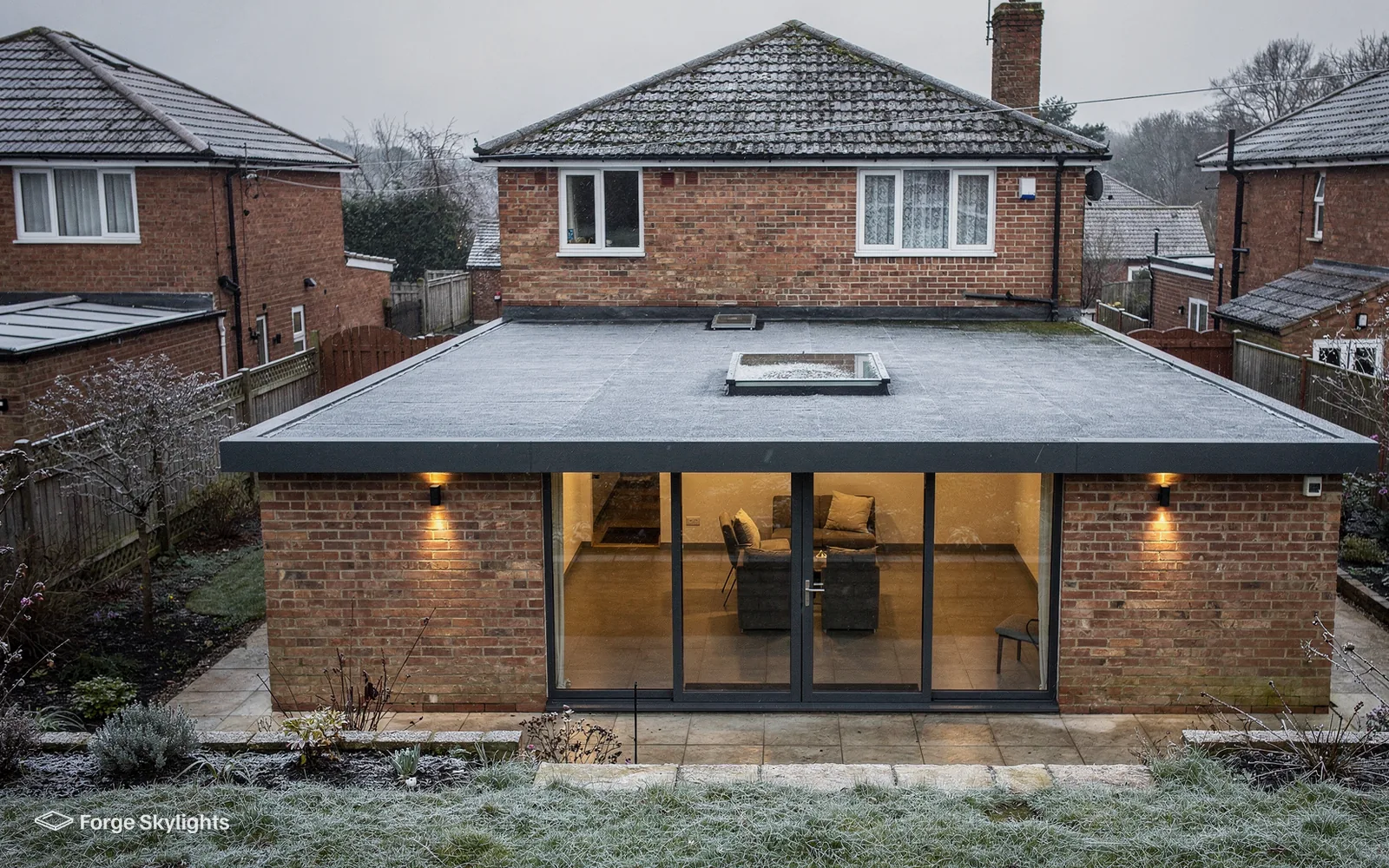 The rear of a brick house with a flat roofed extension, a small rooflight and glazed doors, frost on the lawn