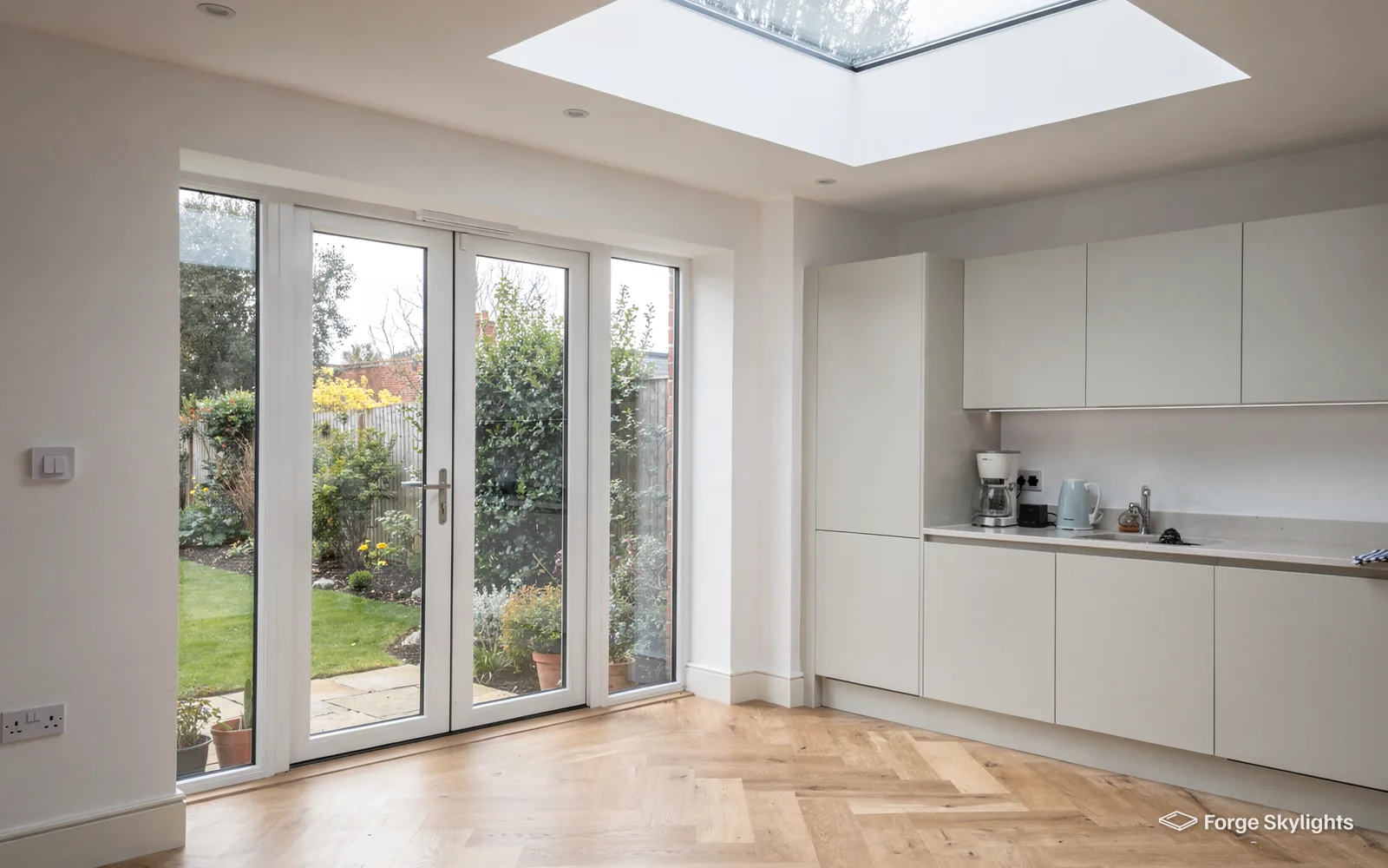 A white kitchen with a rooflight overhead and glazed doors to the garden