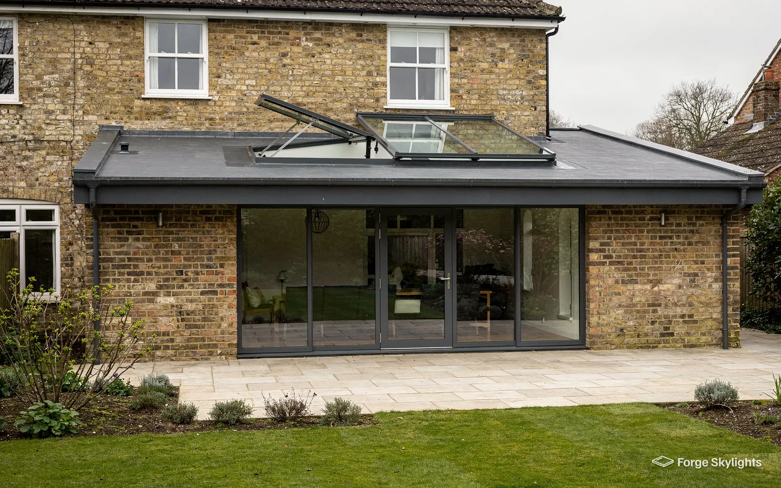 The back of a brick house with a flat-roofed rear extension, an opening rooflight on top and a lawn in front