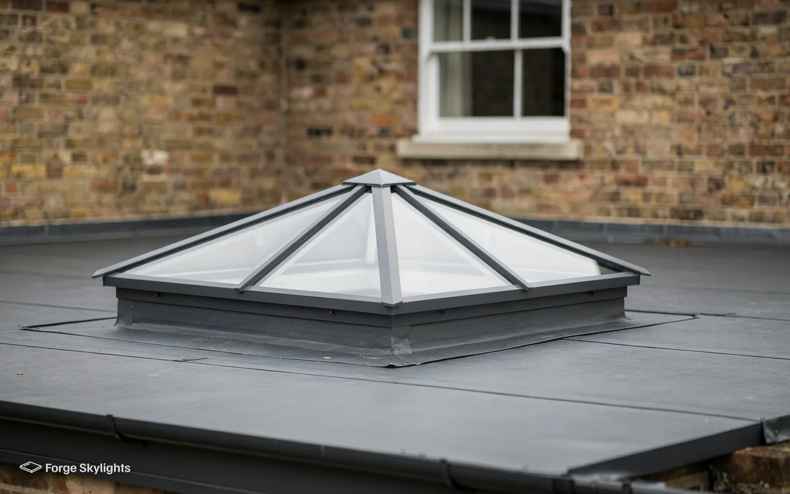 A grey aluminium roof lantern on a flat roof close to a brick wall and sash window