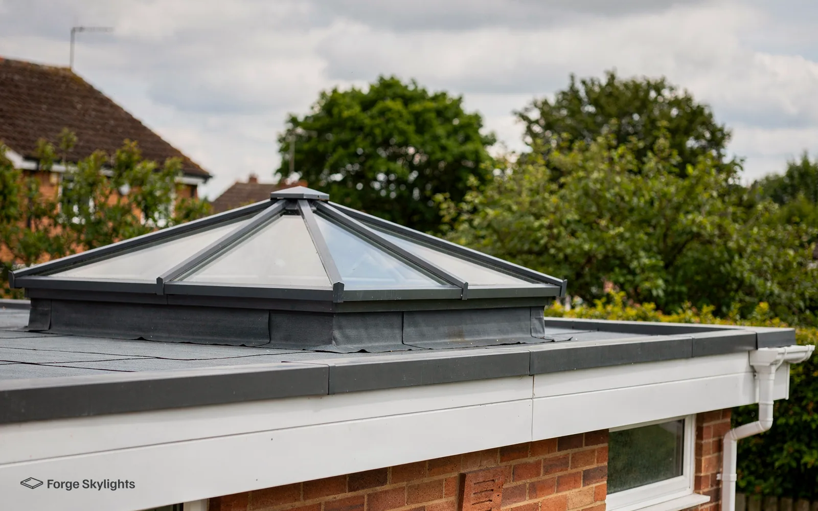 A roof lantern on the flat roof of a red brick single storey extension, trees behind