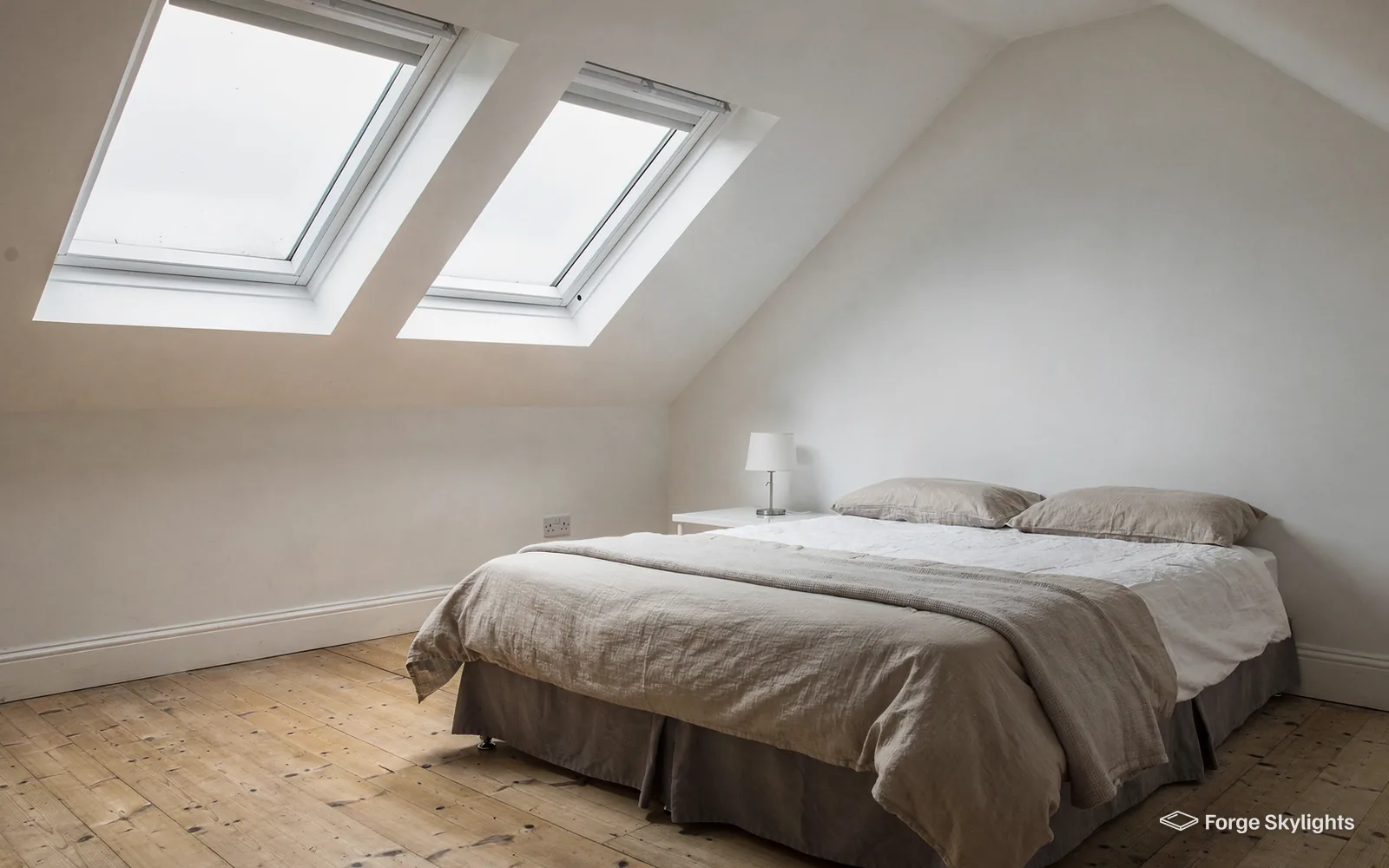 A loft bedroom with two roof windows set in the sloping ceiling above the bed