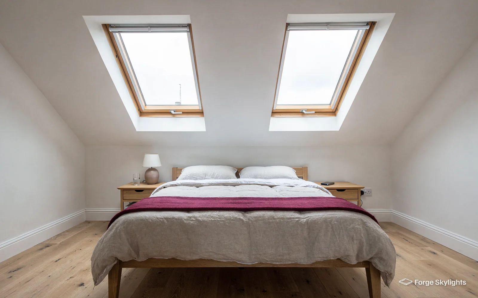 A loft bedroom with a double bed between two pine roof windows