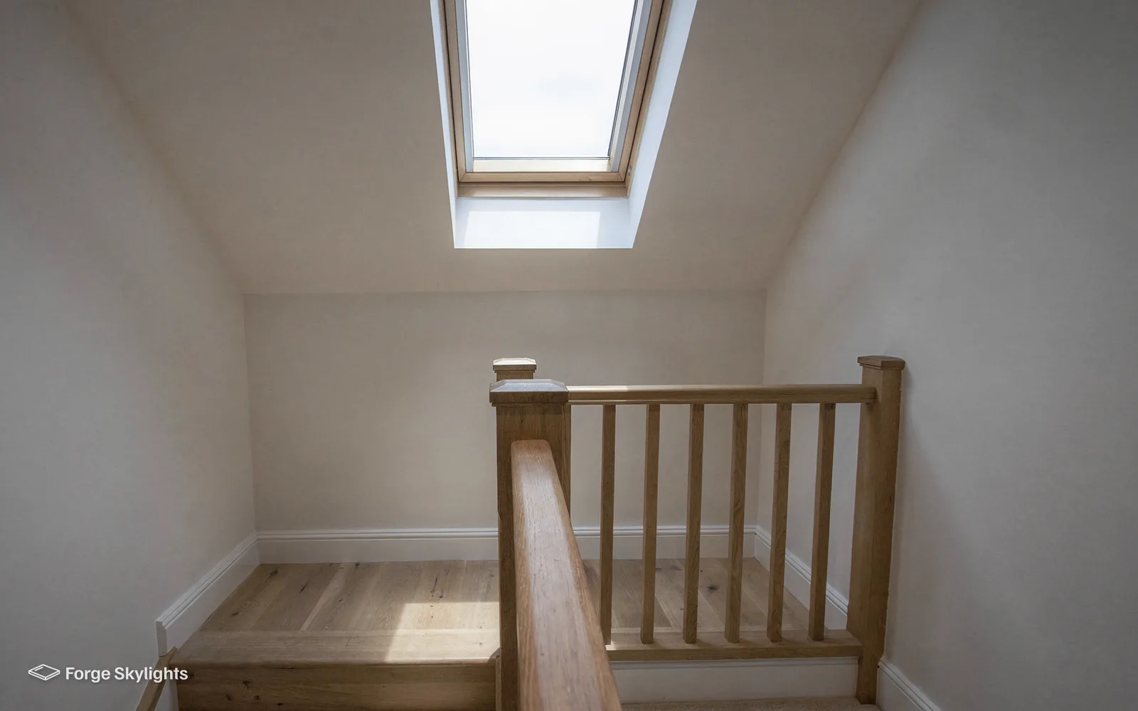 A loft landing with an oak balustrade lit by a roof window above the stairs