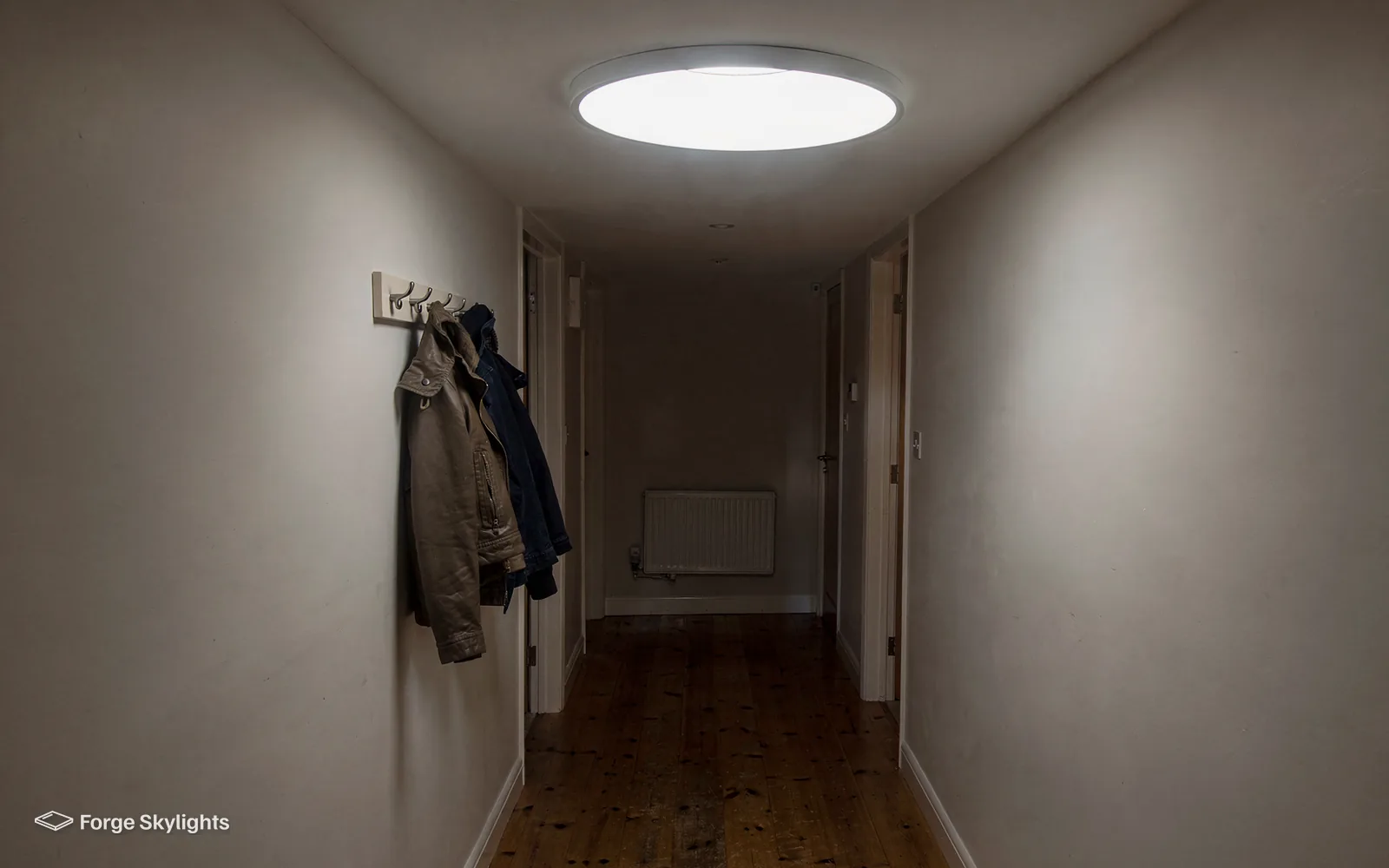 A long corridor lit by a round ceiling diffuser, coats hanging on hooks