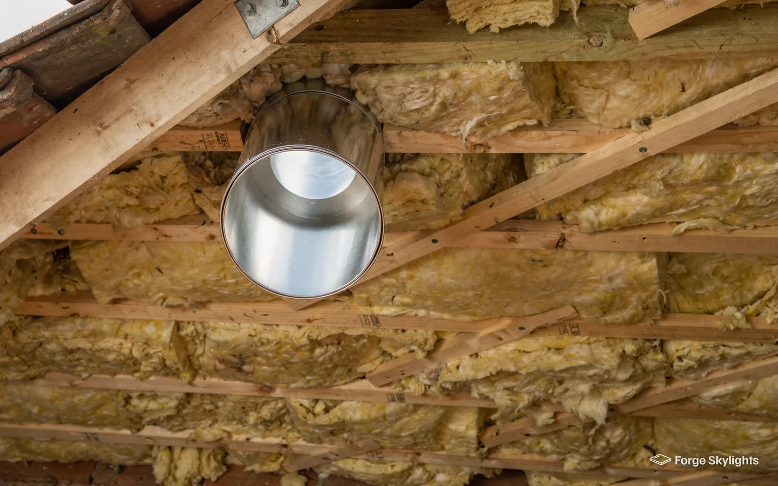 A sun tunnel tube passing through loft insulation between the rafters
