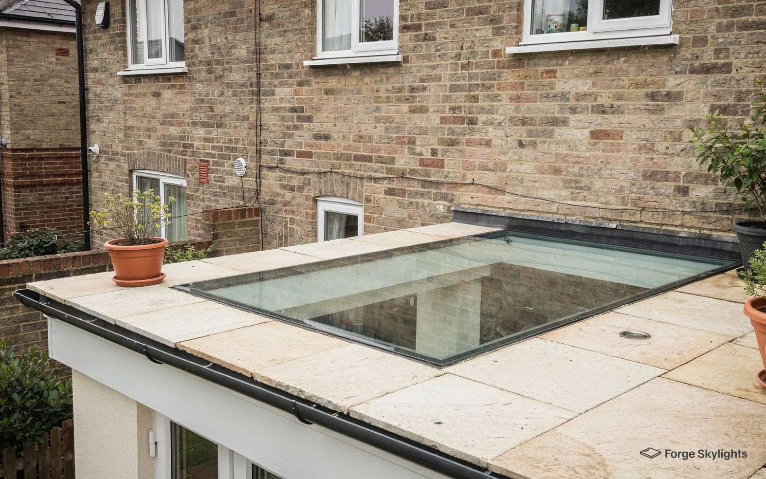 Walk-on glass set in the paved roof of a single storey extension, with planters standing on the paving